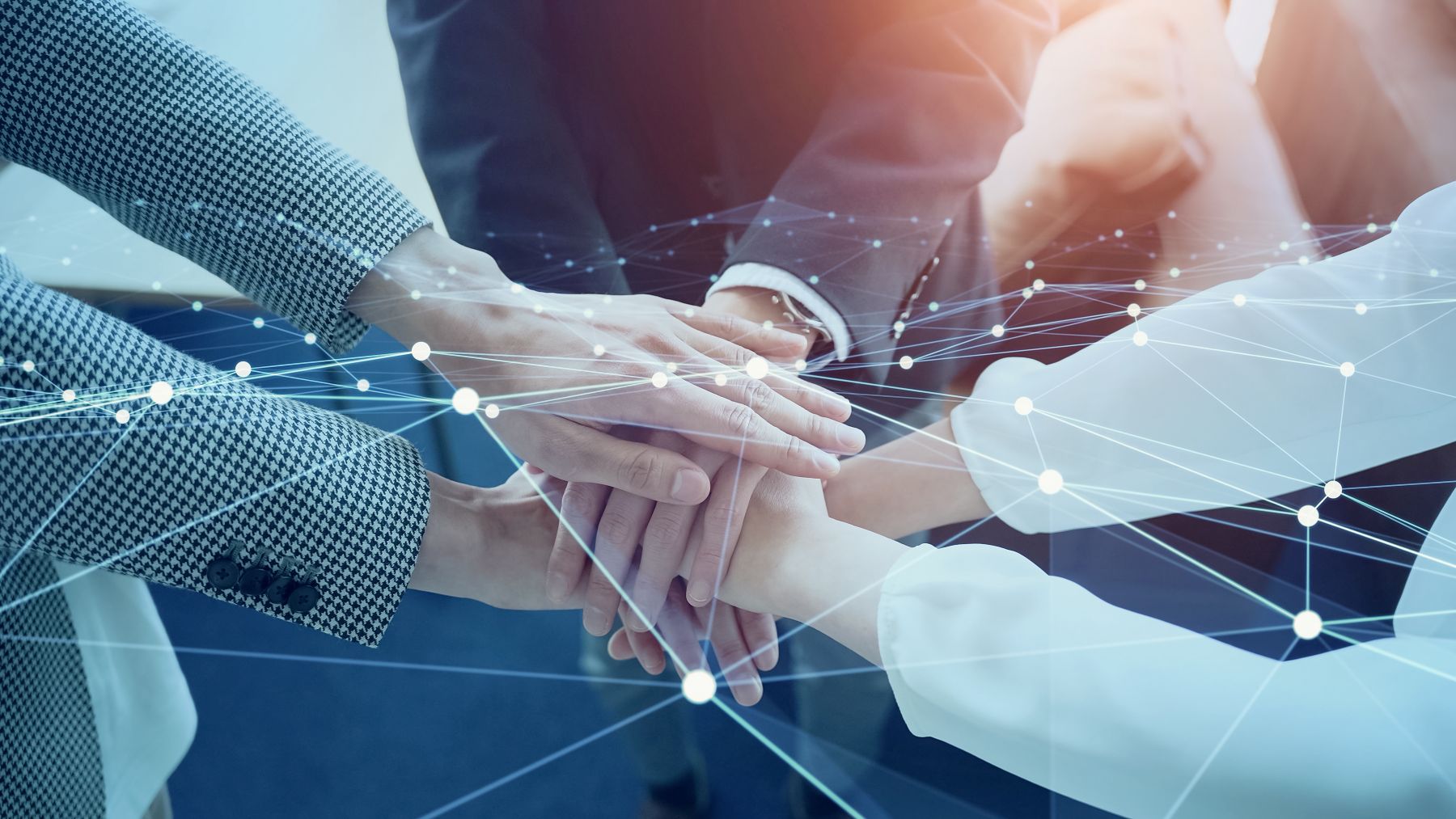 Several people stack their hands together in a gesture of teamwork, with a digital network overlay symbolizing connection and collaboration.