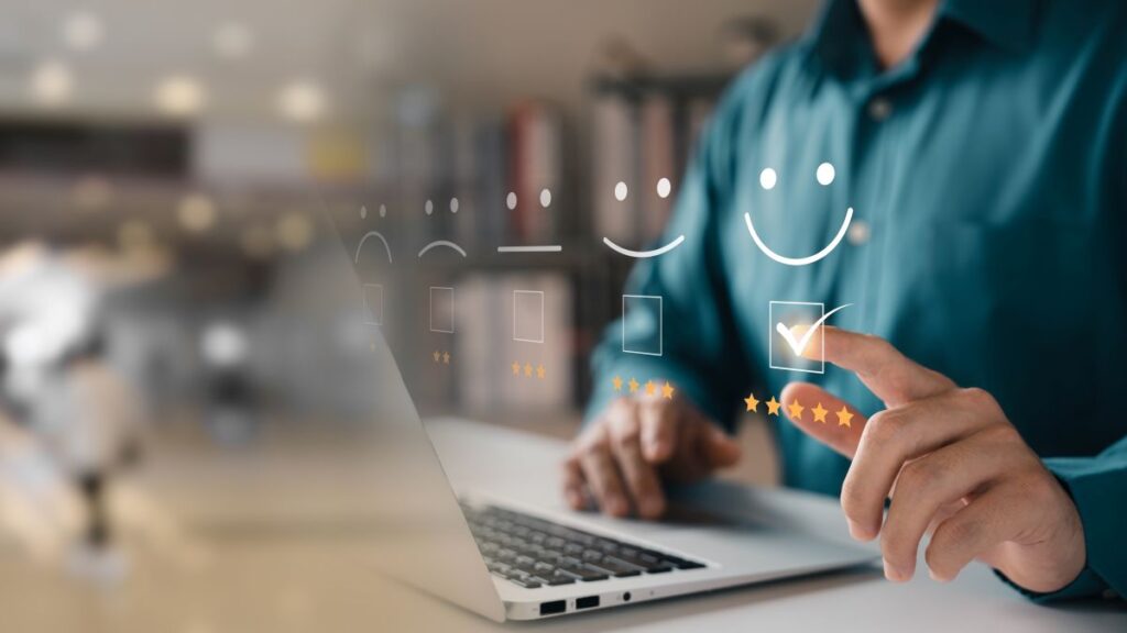 A person uses a laptop, selecting a five-star rating with a smiling face icon on a transparent screen, symbolizing positive customer feedback or satisfaction in a digital setting.